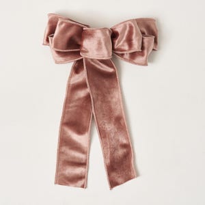 Puede incluir: Un gran lazo de terciopelo rosa empolvado con largas colas. El lazo presenta múltiples capas de tejido suave y texturizado y un delicado borde cosido. Adecuado para envolver regalos o decoración festiva.