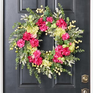 以下が含まれることがあります： ピンクとグリーンの花輪にユーカリの葉と白いベリーが飾られています。花輪は黒いドアにかけられています。