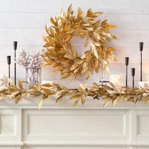 May include: Gold leaf garland and wreath on a white mantel with black candle holders and white candles.