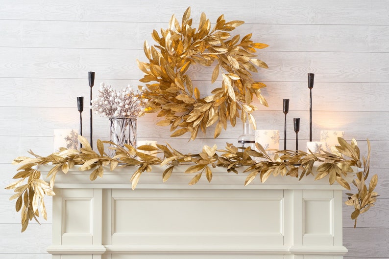 May include: Gold leaf garland and wreath on a white mantel with black candle holders and white candles.