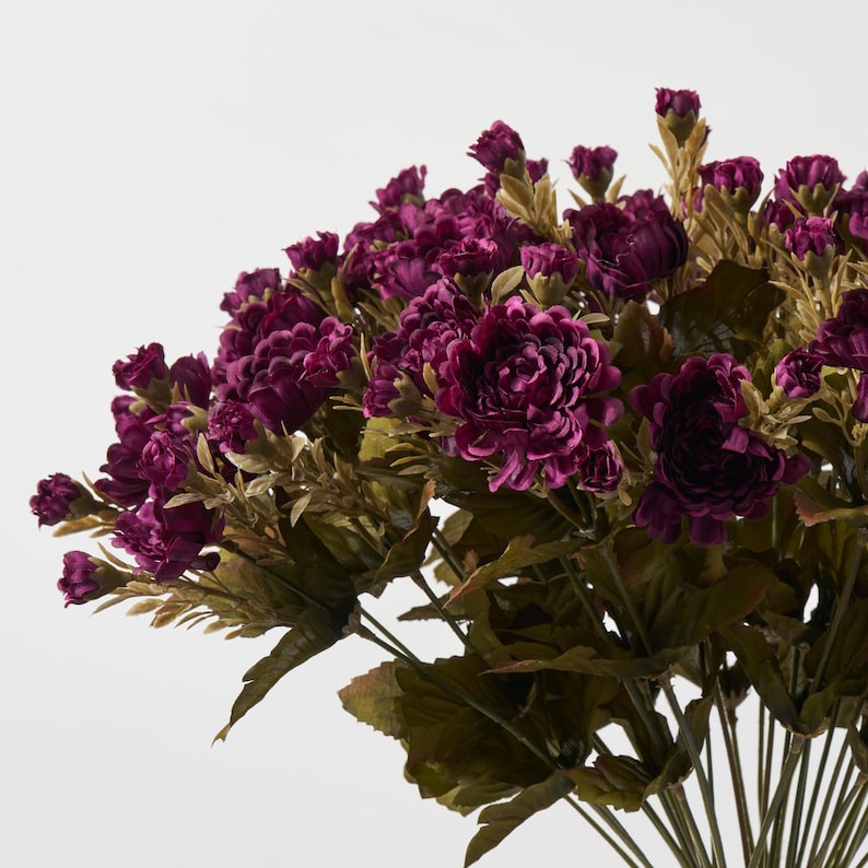 May include: A bouquet of artificial flowers with deep purple blooms and green leaves.