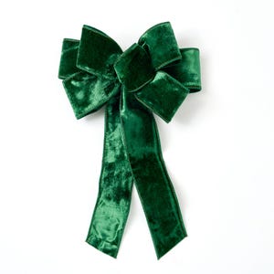 Puede incluir: Un gran lazo de terciopelo verde con colas largas. El lazo está atado en un estilo clásico y simétrico.