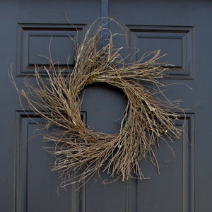 May include: A brown twig wreath hangs on a black door. The wreath is made of natural branches and has a rustic look.