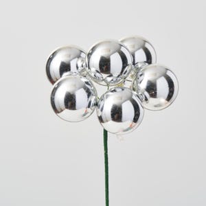 May include: A silver floral pick with six shiny, round ornaments. The pick is green and has a wire stem.