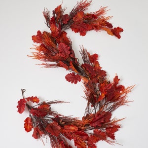 May include: A red and orange autumn garland with oak leaves and pine needles. The garland is ideal for decorating for the autumn season.