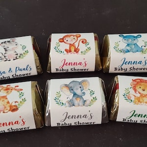 May include: Six small chocolate bars wrapped in gold foil with labels featuring watercolor illustrations of various animals, including a zebra, monkey, rhinoceros, giraffe, elephant, and lion. The labels also include the text "Jenna's Baby Shower" or "Lisa & Paul's Baby Shower".