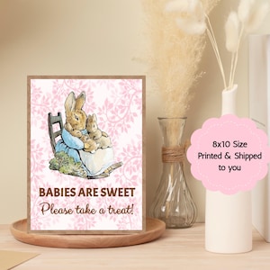 May include: A framed print featuring a watercolor illustration of a mother rabbit and a baby rabbit. The print has a pink floral background and text that reads "BABIES ARE SWEET Please take a treat!" The print is 8x10 inches.