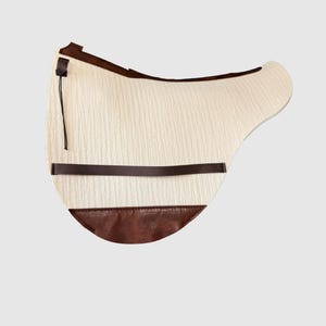 May include: A white sheepskin saddle pad with a brown leather trim and a black strap.