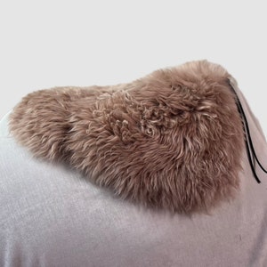 May include: A light brown sheepskin saddle pad with black leather ties.