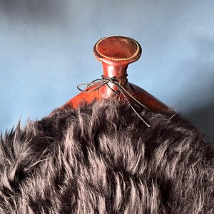 May include: A brown leather saddle with a black sheepskin seat. The saddle has a decorative leather top with a stitched design.
