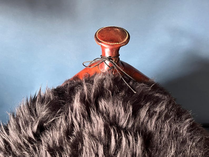 May include: A brown leather saddle with a black sheepskin seat. The saddle has a decorative leather top with a stitched design.
