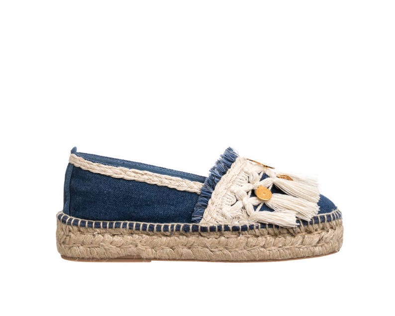 May include: Blue denim espadrille shoes with white crocheted trim and gold button accents. The shoes have a jute sole and a tassel detail.