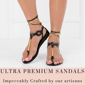 May include: Black leather sandals with gold bead embellishments and ankle straps. The sandals have a simple design and are perfect for summer.