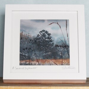 May include: A framed watercolor painting of a landscape with tall grasses and trees in shades of blue and brown. The title "A Sense of September" is written in the bottom left corner, and the artist's signature is in the bottom right corner.