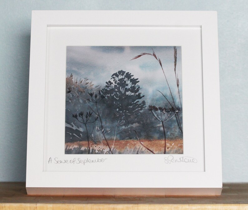 May include: A framed watercolor painting of a landscape with tall grasses and trees in shades of blue and brown. The title "A Sense of September" is written in the bottom left corner, and the artist's signature is in the bottom right corner.