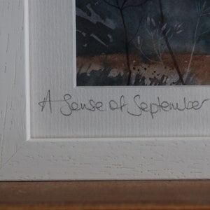 May include: A white framed watercolor painting with a dark blue and brown landscape. The painting is signed "A Sense of September".