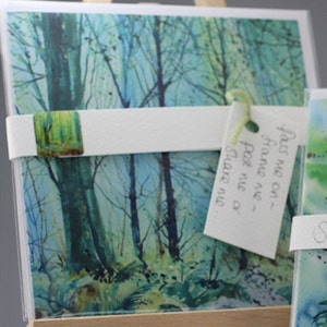 May include: A watercolor painting of a forest scene with tall trees and a blue sky. The painting is on a card with a tag that says "Press me on - frame me - post me - share me".