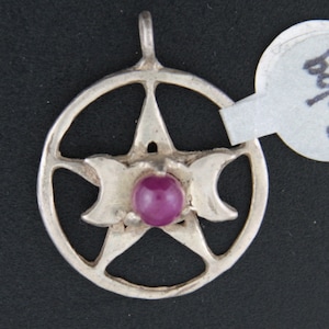 May include: A silver pendant with a pentagram design and a purple gemstone in the center. The pendant is on a black background.