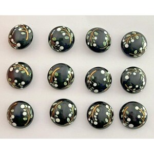 May include: Twelve black ceramic buttons with white and gold floral designs. The buttons are round and have a glossy finish.