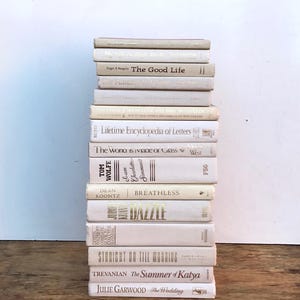 May include: A stack of 14 off-white books with gold lettering on the spines. The titles include "The Good Life", "Lifetime Encyclopedia of Letters", "The World is Iviage of Glass", "Breathless", "Dazzle", "Straight on Till Morning", "The Summer of Katya", and "The Wedding".