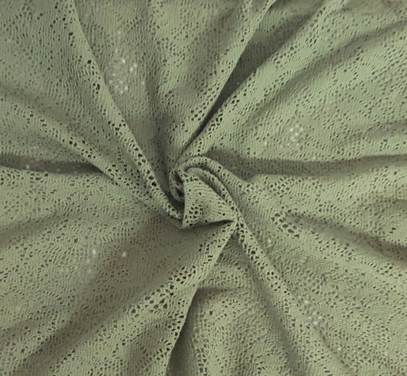 May include: A close-up of a sage green crocheted fabric with a delicate openwork pattern.