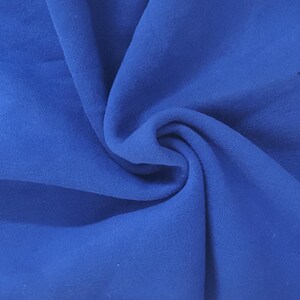 May include: A solid royal blue fabric with a soft, matte texture. The material is gathered in the center, creating deep, flowing folds and shadows that highlight the consistent, vibrant blue color across the entire surface of the textile.