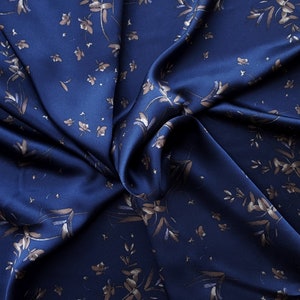 May include: A close-up of a navy blue fabric with a subtle floral pattern in a lighter shade of blue. The fabric is smooth and silky, with a slight sheen.