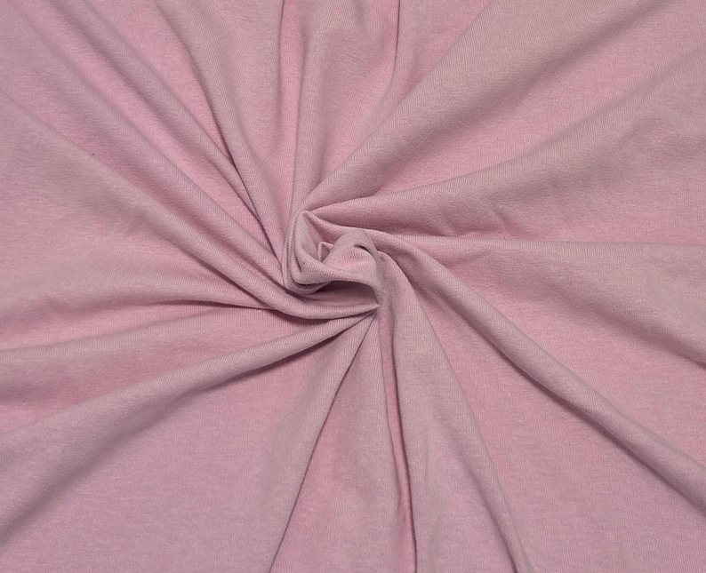 May include: A solid light pink fabric with a soft, matte texture. The material is gathered in the center, creating natural folds and drapes that radiate outward, showcasing the consistent pastel pink color and the fine weave of the textile.
