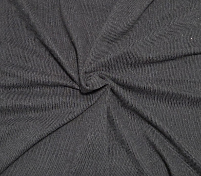 May include: Close-up of a dark gray fabric with a textured surface. The fabric is gathered in a swirl, creating folds and shadows. The material appears to be soft and flexible, suitable for clothing or other textile projects.