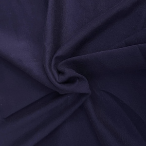 May include: Close-up of a dark blue fabric with a smooth, slightly textured surface. The fabric is folded and draped, showing its soft and flexible nature.