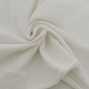 May include: Close-up of a white fabric with a soft, textured surface. The fabric is draped and folded, creating a swirling pattern. The edges of the fabric are finished with a hem. The material appears to be a soft, plush textile.