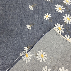 May include: Two pieces of denim fabric with a white daisy pattern. One piece is dark blue and the other is light blue.