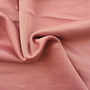 May include: Close-up of a soft, pink fabric with a subtle textured pattern. The fabric is draped and folded, showcasing its smooth and luxurious feel.