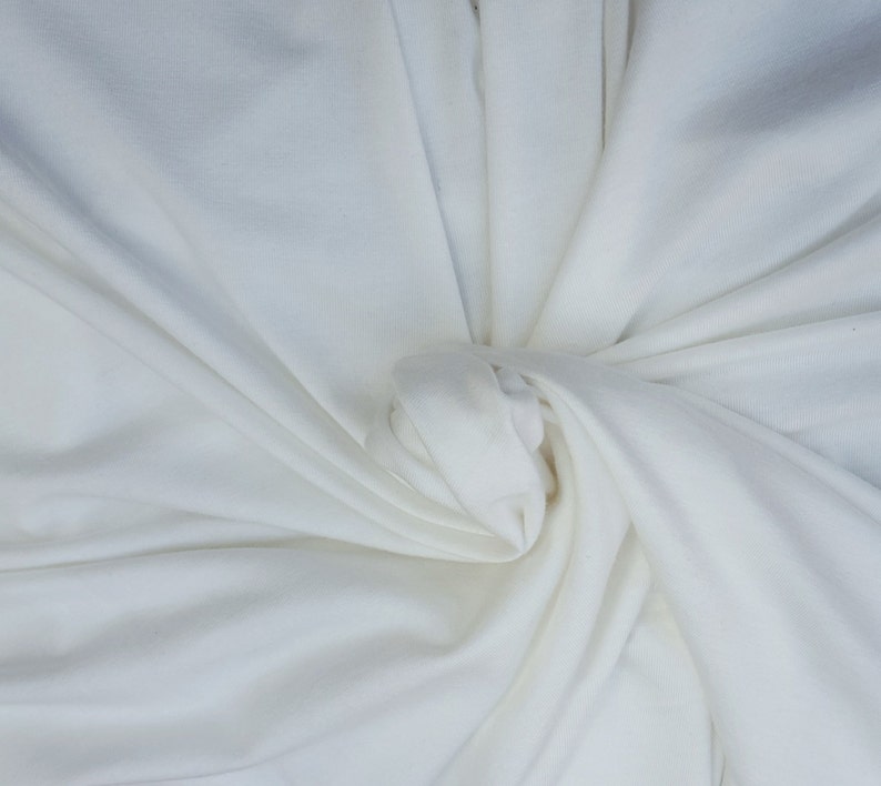 May include: White fabric with a soft, smooth texture. The fabric is bunched up in the center, creating a swirling pattern.