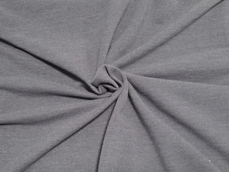 May include: Close-up of gray fabric with a textured surface. The fabric is gathered in the center, creating a swirling pattern. The material appears to be soft and pliable, with visible woven threads. The overall color is a muted gray.