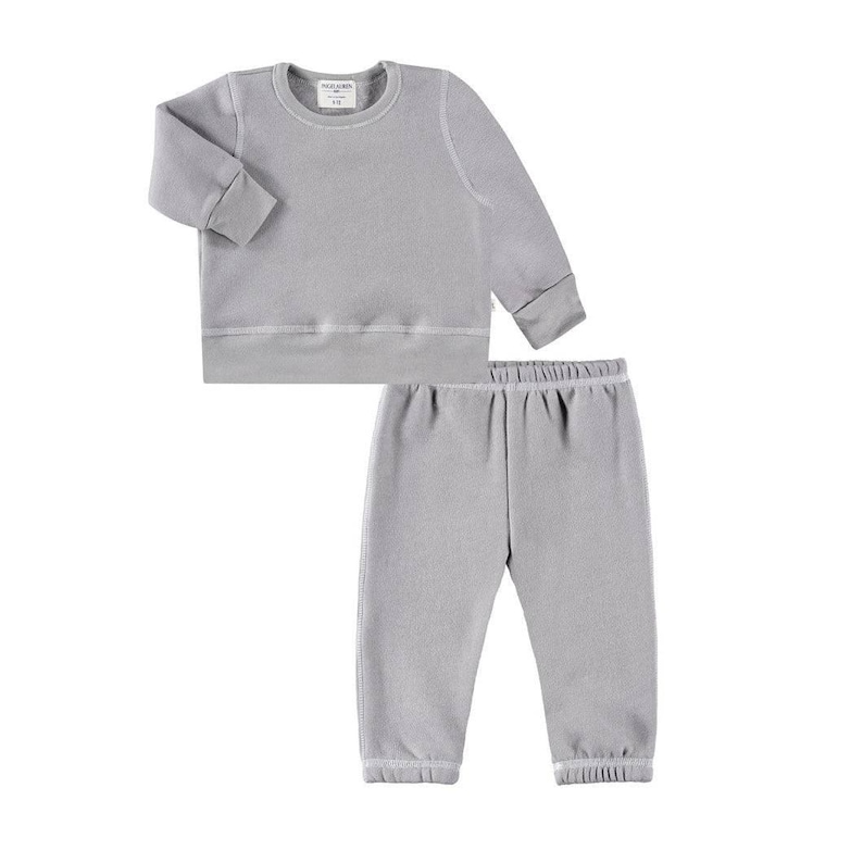 May include: A light gray, two-piece children's outfit. The set includes a long-sleeved sweatshirt and matching sweatpants. The sweatshirt has a crew neck and ribbed cuffs and hem. The sweatpants have an elastic waistband and ribbed cuffs.