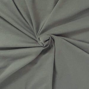 Puede incluir: Una tela de color gris medio s&oacute;lido con una textura suave y mate. El material est&aacute; reunido en el centro, creando una serie de pliegues radiantes y sombras suaves que se extienden hacia los bordes del marco, resaltando la ca&iacute;da.