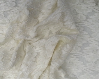 May include: Off-white lace fabric with a floral leaf pattern. The delicate material is draped, creating soft folds and shadows. The texture appears slightly textured, adding depth to the design. Ideal for apparel or craft projects.