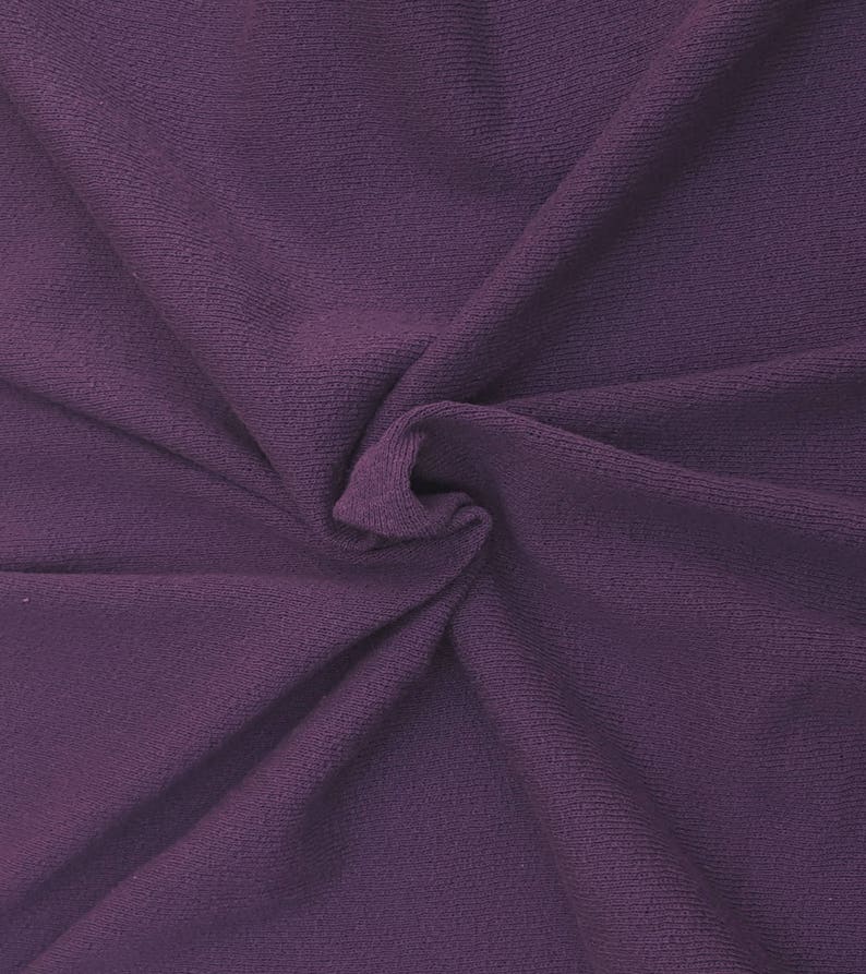 May include: A close-up of a soft, purple fabric with a textured, ribbed surface. The fabric is folded and draped, creating a smooth, flowing texture.