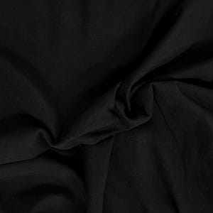 May include: A solid black fabric with a smooth, matte texture. The material is draped in soft, organic folds, creating deep shadows and subtle highlights across the surface. The textile appears opaque and uniform in its deep, dark black color.