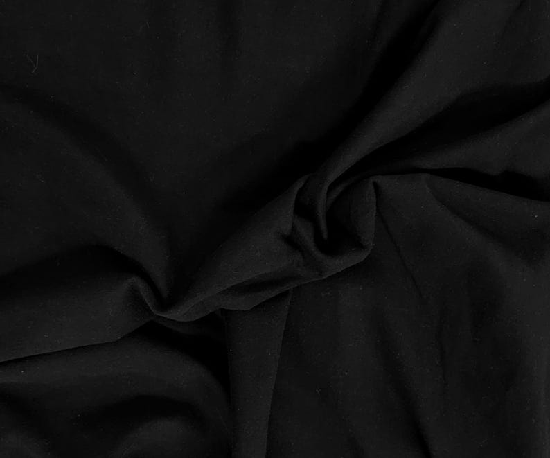 May include: A solid black fabric with a smooth, matte texture. The material is draped in soft, organic folds, creating deep shadows and subtle highlights across the surface. The textile appears opaque and uniform in its deep, dark black color.