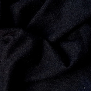 May include: Close-up of a dark blue fabric with a textured surface. The fabric is folded and wrinkled, creating a dramatic and abstract background.