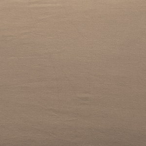 May include: A close-up of a smooth, light brown fabric with a subtle texture. The fabric has a slightly wrinkled appearance.