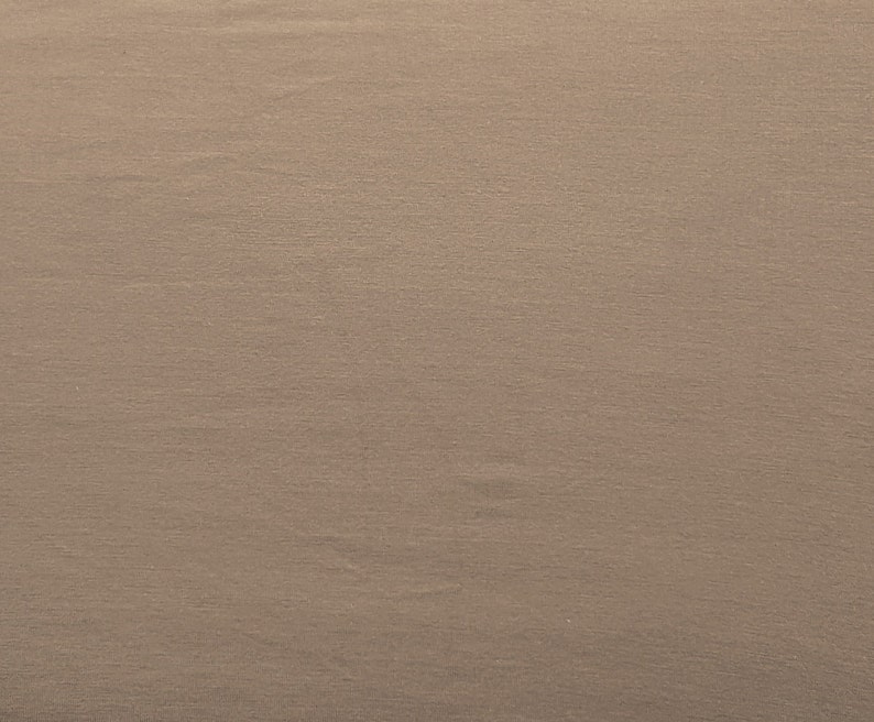 May include: A close-up of a smooth, light brown fabric with a subtle texture. The fabric has a slightly wrinkled appearance.