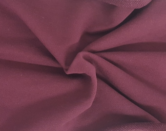 May include: Close-up of a folded piece of burgundy fabric. The fabric has a soft texture and a visible knit pattern. The edges are finished with a darker, ribbed trim. The overall appearance suggests a garment or textile material.