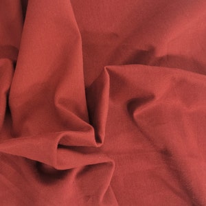 Pu&ograve; includere: Primo piano di un tessuto rosso scuro con una superficie testurizzata. Il tessuto &egrave; piegato e drappeggiato, creando pieghe e curve morbide.