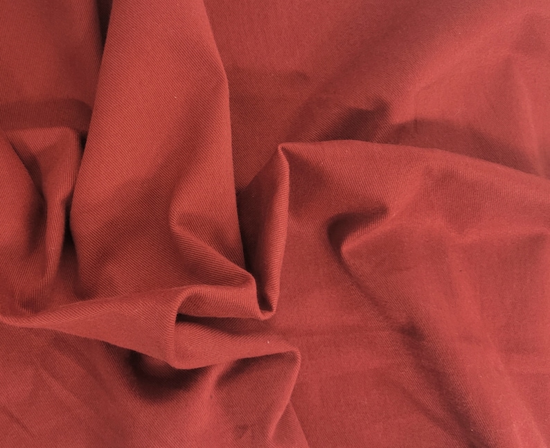 Pu&ograve; includere: Primo piano di un tessuto rosso scuro con una superficie testurizzata. Il tessuto &egrave; piegato e drappeggiato, creando pieghe e curve morbide.