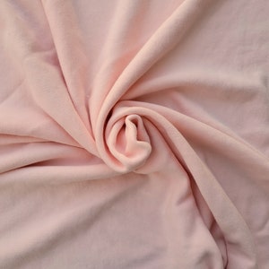 May include: A close-up shot of a soft, light pink fabric with a swirling pattern. The fabric is draped and folded, creating a textured, almost floral appearance. The color is a delicate, muted pink.