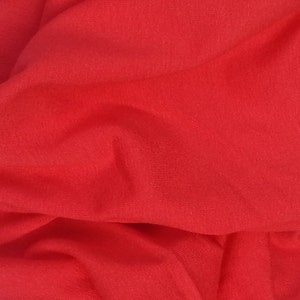 May include: A close-up of a red fabric with a smooth texture. The fabric is folded and draped, creating soft folds and curves.