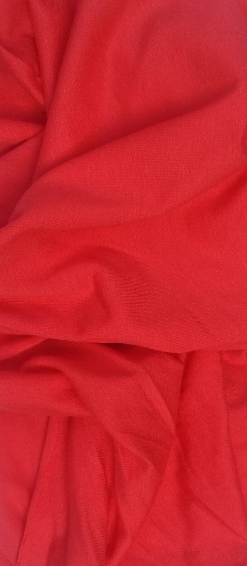 May include: A close-up of a red fabric with a smooth texture. The fabric is folded and draped, creating soft folds and curves.